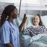 Pediatric nurse giving a high-five to a child in a hospital bed