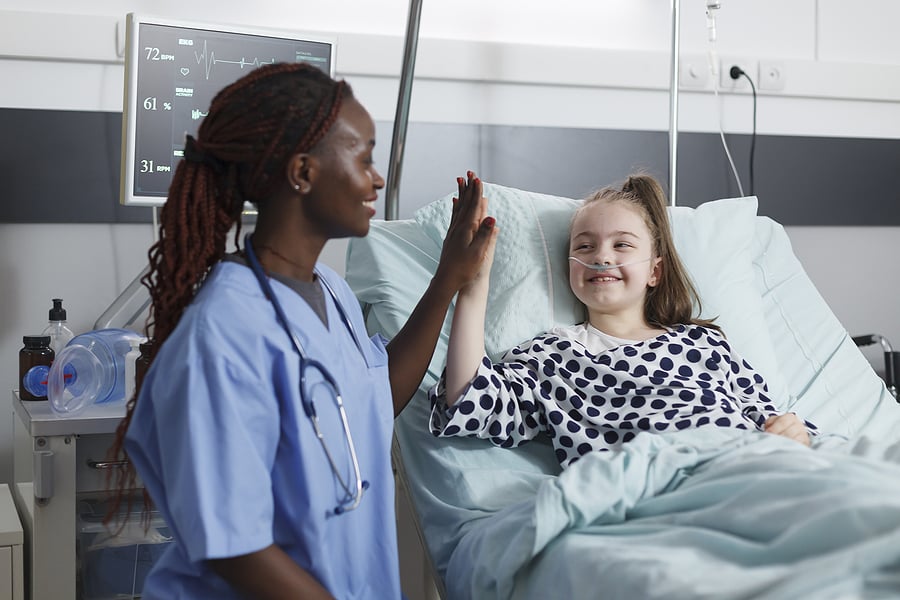 Pediatric nurse giving a high-five to a child in a hospital bed