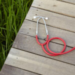 Red stethoscope on a grassy dock